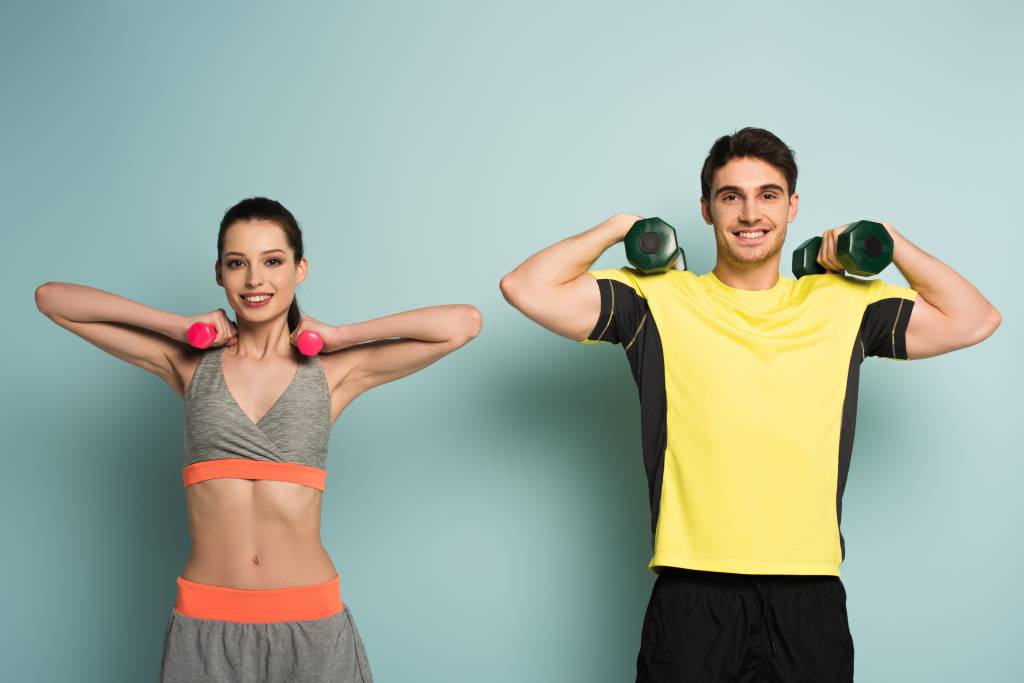 cheerful athletic couple training with dumbbells on blue