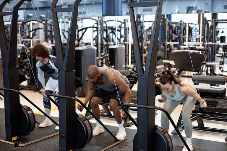 Full length portrait of group of people using exercise machines during strength training in gym